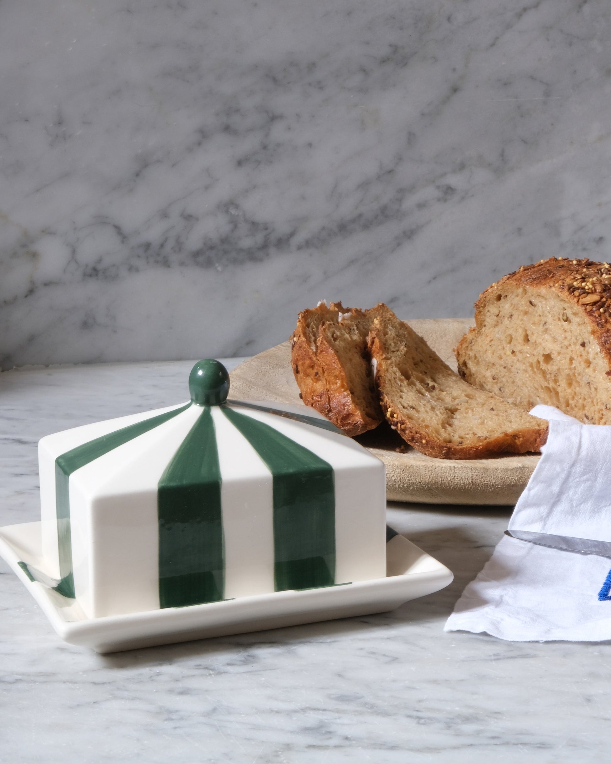 Issy Granger Circus Striped Butter dish with green and white stripes on a marble surface with bread and a knife