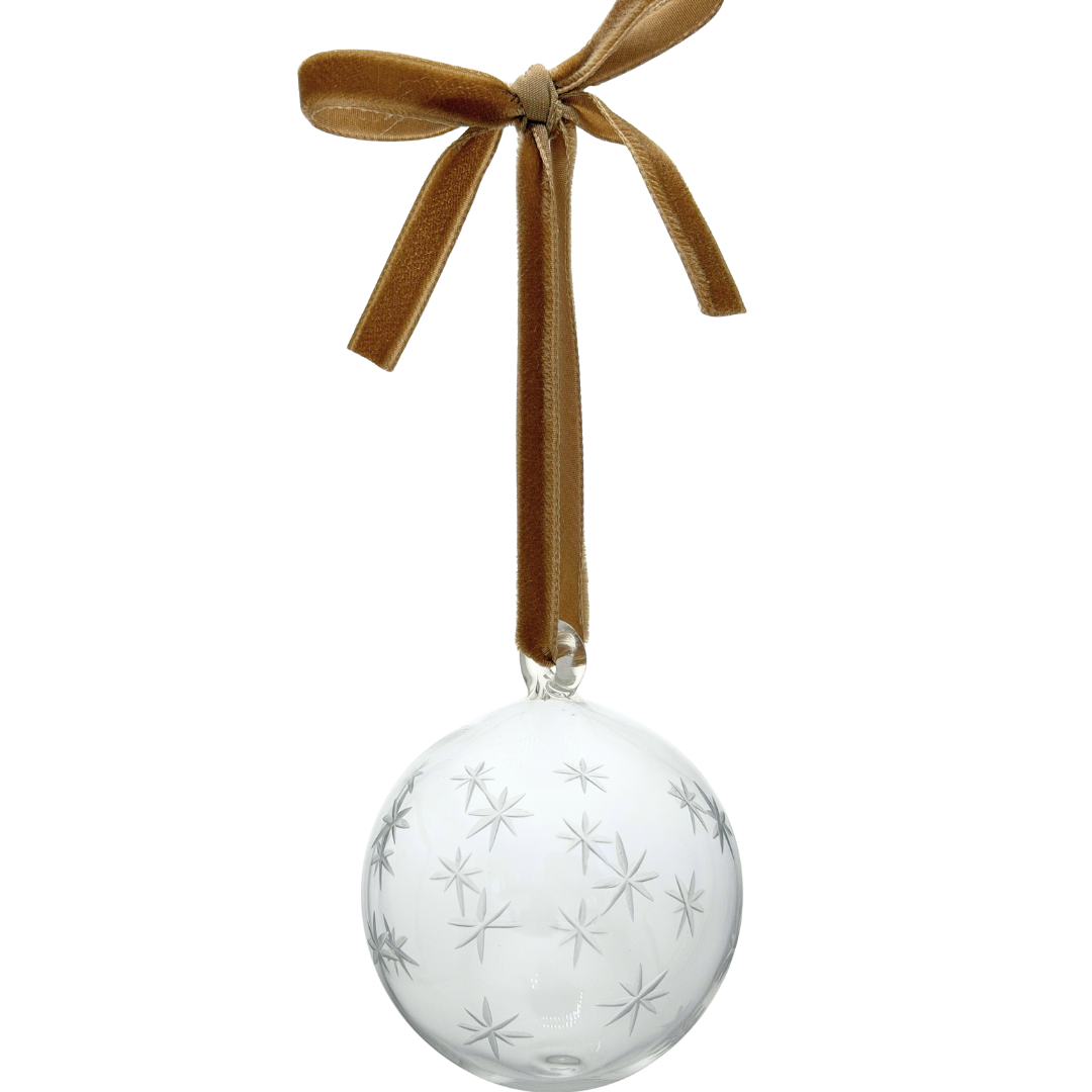 A clear glass Christmas ornament bauble with etched stars, hanging from a gold velvet ribbon tied in a bow. christmas tree decoration 