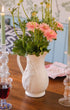 White pitcher with flowers, two lit candles, and a glass of red wine on a wooden table. Issy Granger